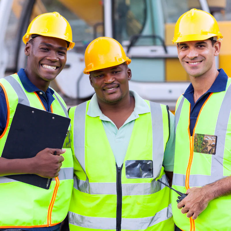 Three construction workers wearing yellow hard hats and safety vests, with one holding a clipboard.