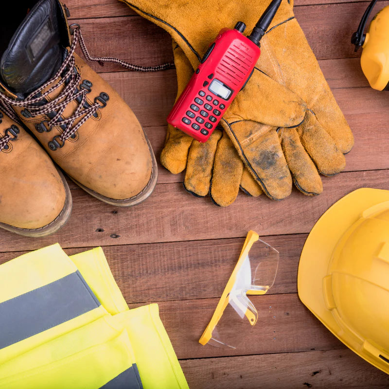 Work boots, gloves, radio, safety glasses, and hard hat on a wooden surface