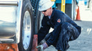 Person in a hard hat and work coveralls inspecting a truck tire.